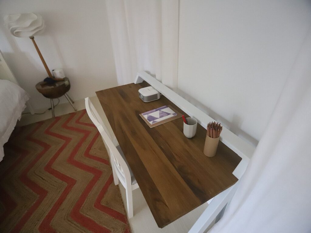 USVI IMG 5179 - Wooden desk with a notebook and pencils sits beside a white chair next to a bed with a chevron