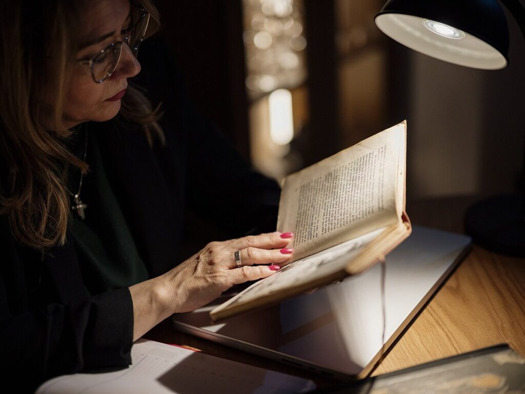 Middle-aged businesswoman reading a book under warm light in a quiet room during evening hours, surrounded by