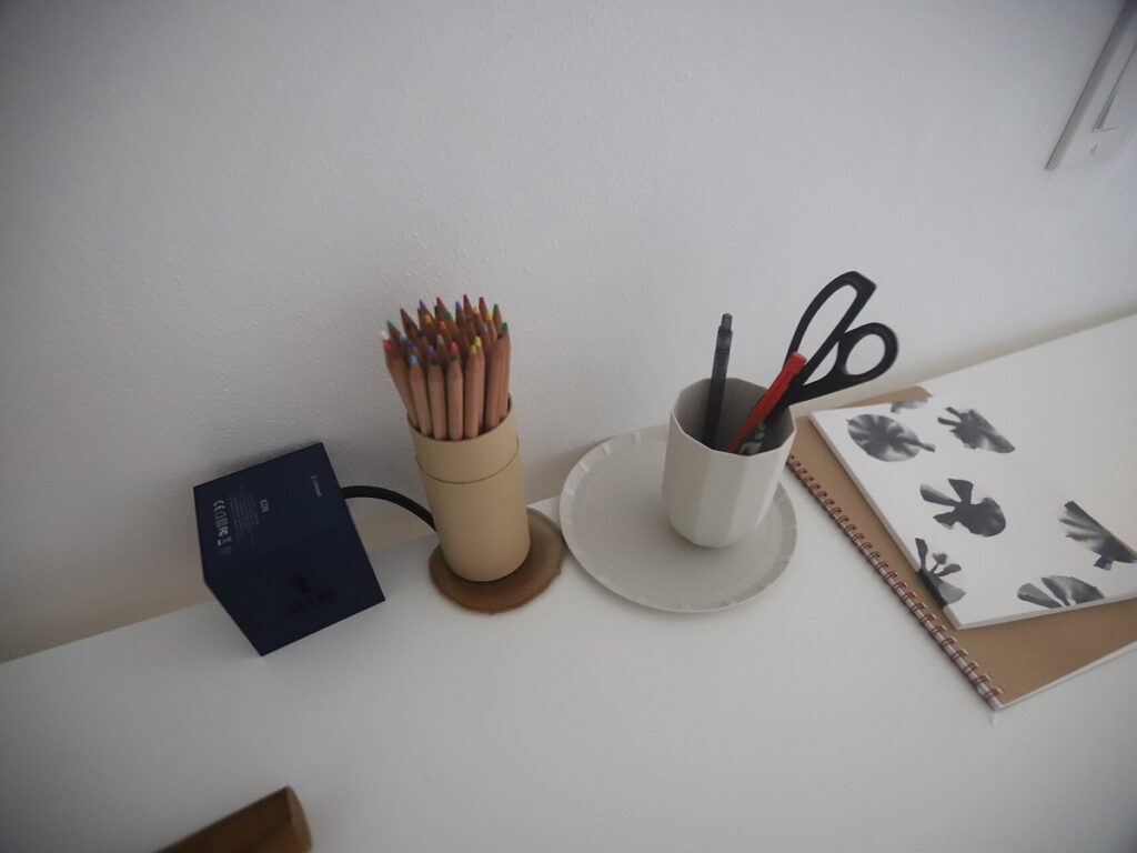 USVI IMG 5202 - Minimalist desk with colorful pencils in a cardboard holder a cup holding pens and scissors an